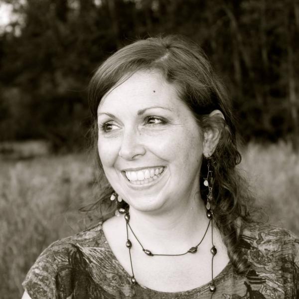 Laura Read smiling while looking off to the right, in a field, with dangly earrings and necklaces