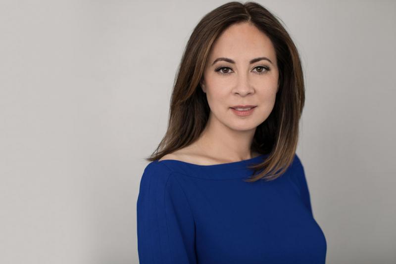 Portrait of Paisley Rekdal in front of a light backdrop wearing a jewel-toned blue blouse.