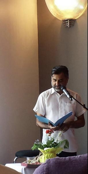 {hoto of Phinder Dulai speaking at a microphone, looking down at a folder in his hands.