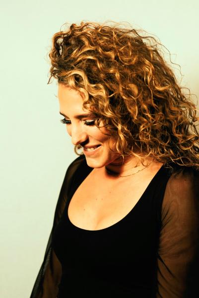 Portrait of Taneum Bambrick looking down while smiling, wearing a black blouse