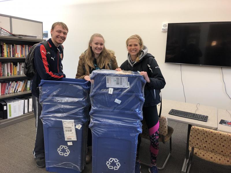 Three Environmental Club members pose with new blue recycle bins.