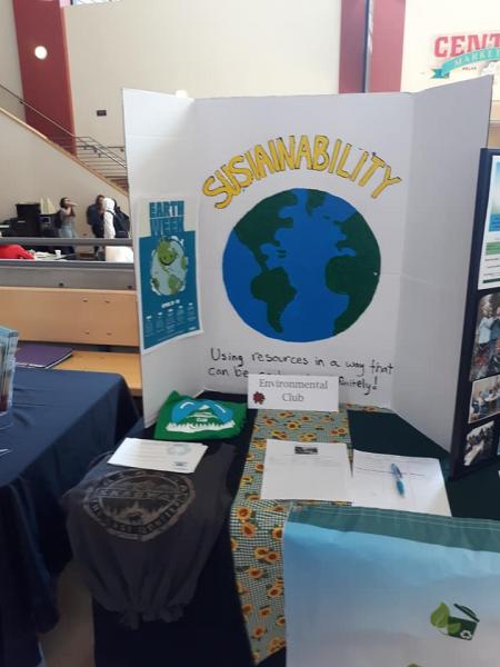 CWU Environmental Club displays items on a table in the SURC.  One of the items is a white tri-fold standing poster that says sustainability in yellow and a blue and green earth.