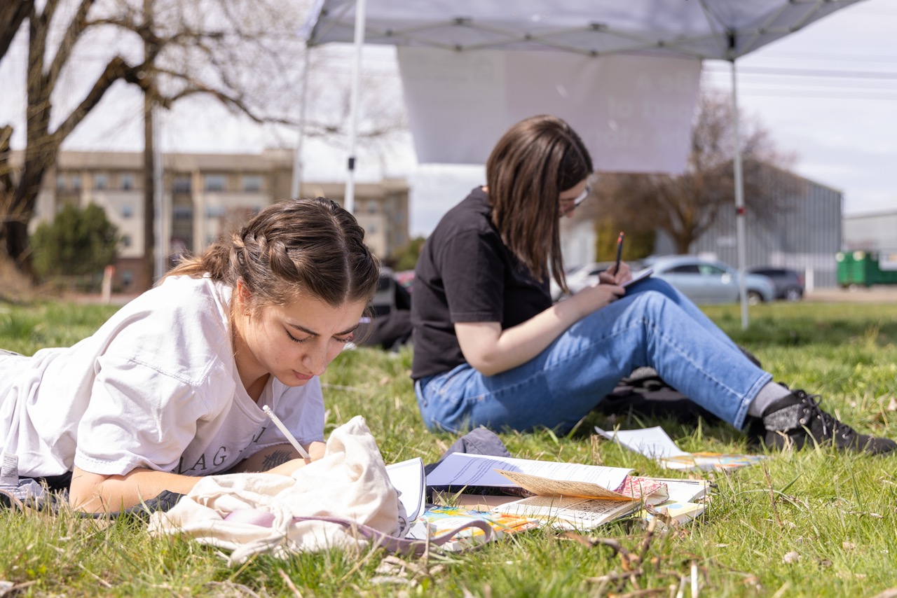 Two students reading and writing in the grass. 