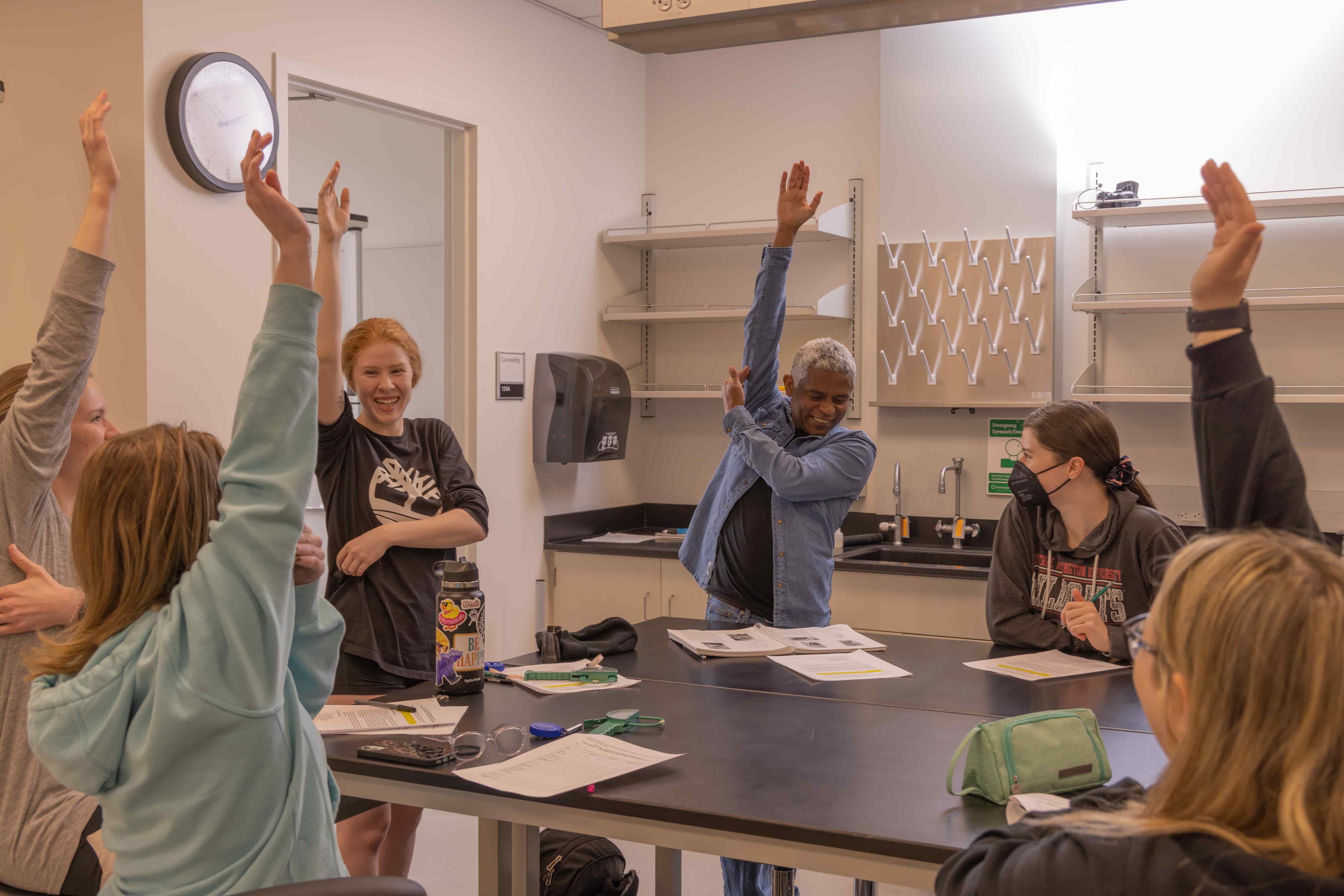 A CWU professor smiles and points to a muscle in his arm while raising his hand for his class to see.