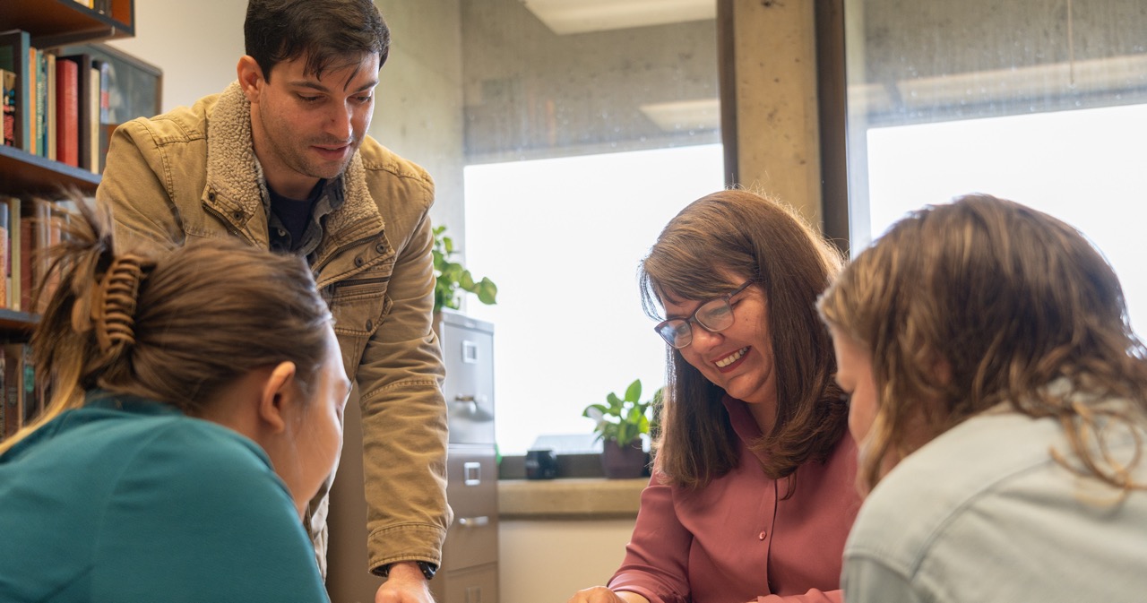 Students standing beside a professor looking at a history book