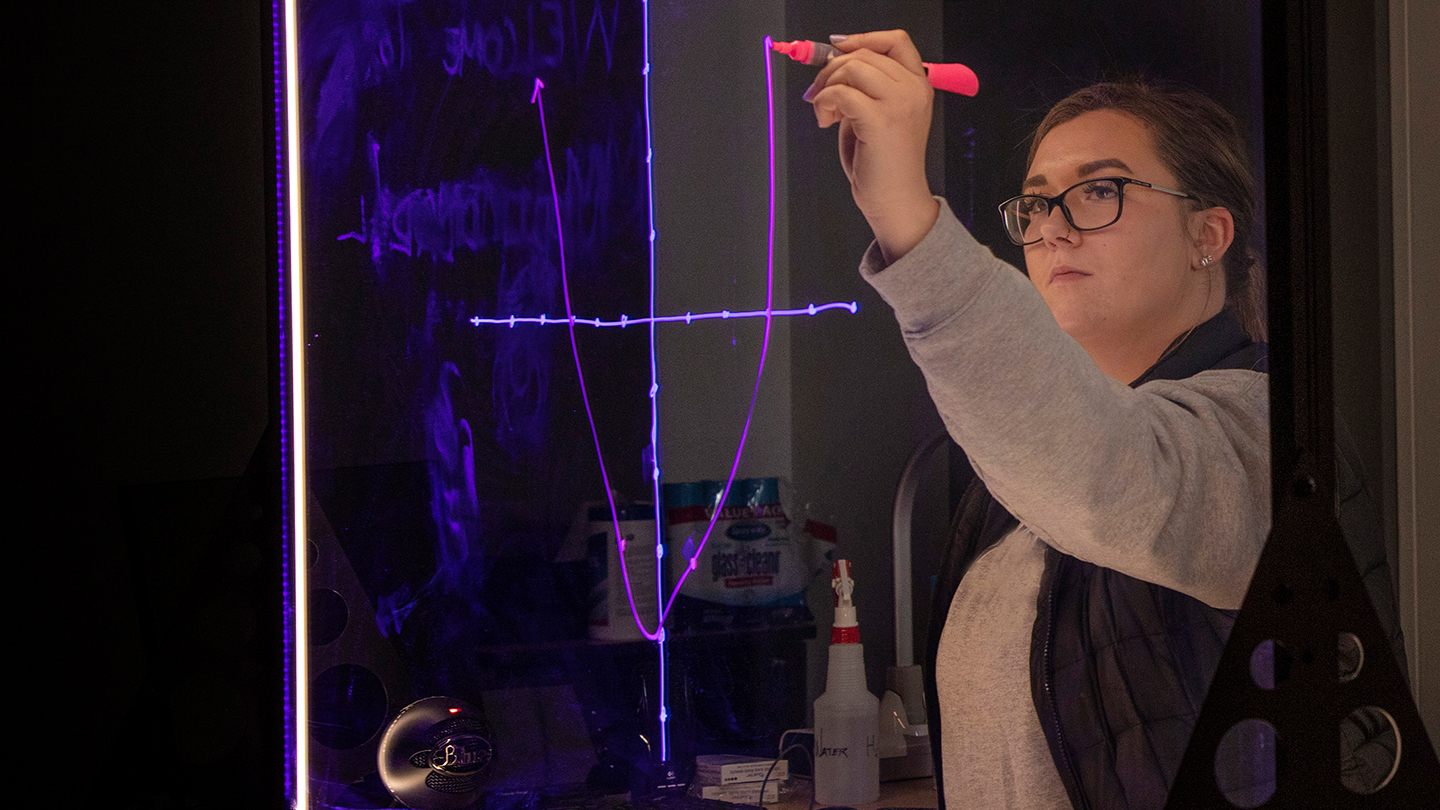 Student writing on high-tech whiteboard that glows