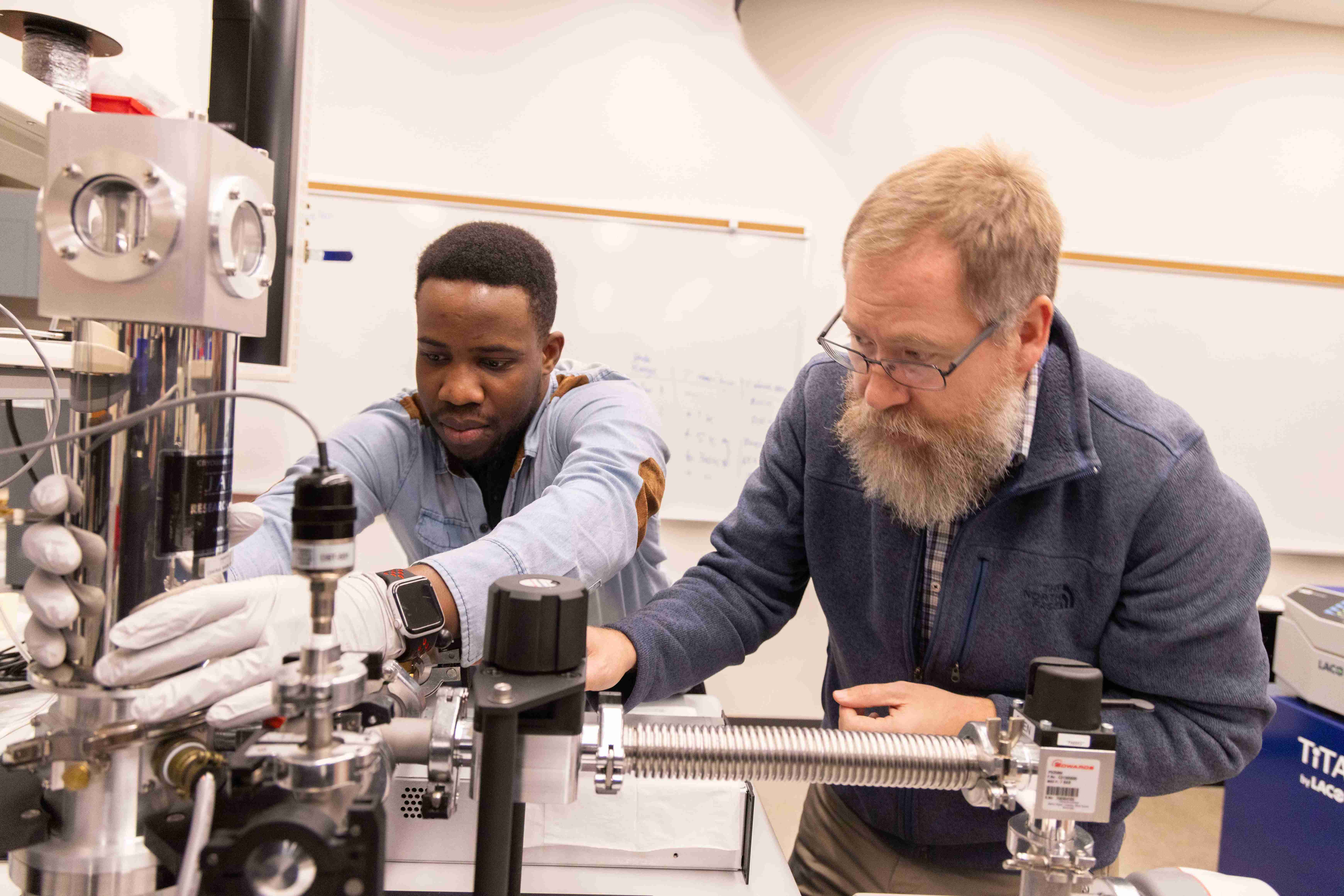 Student adjusting lab equipment and professor watching intently