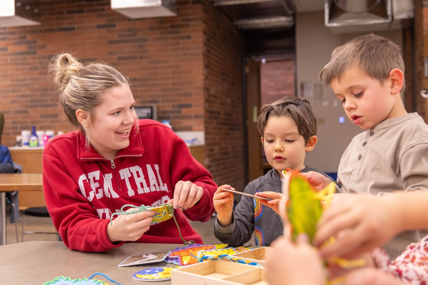 Student with a big smile looking at two young children working on their craft project