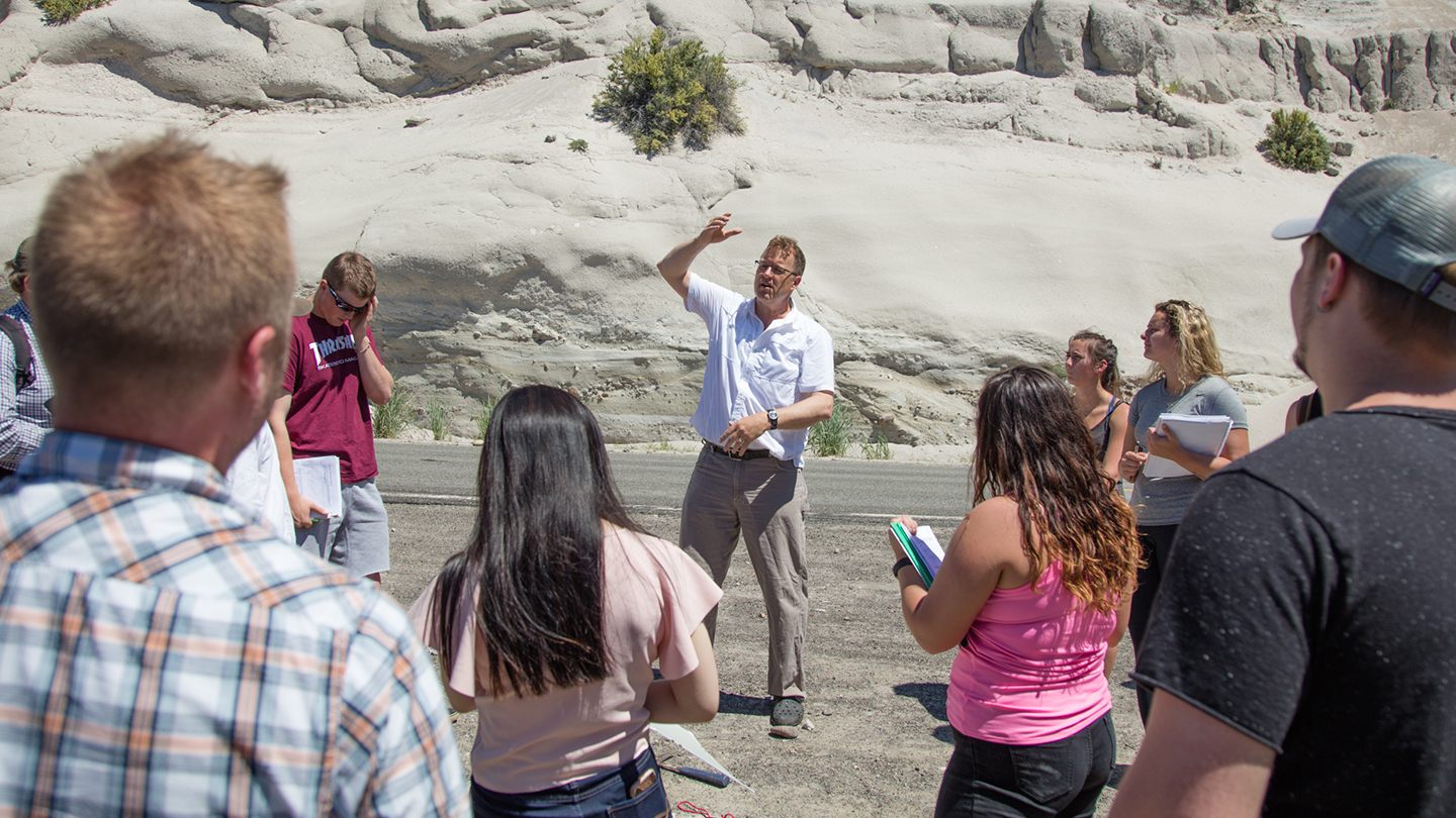 Professor standing and talking in front of students outside in front of rock formations