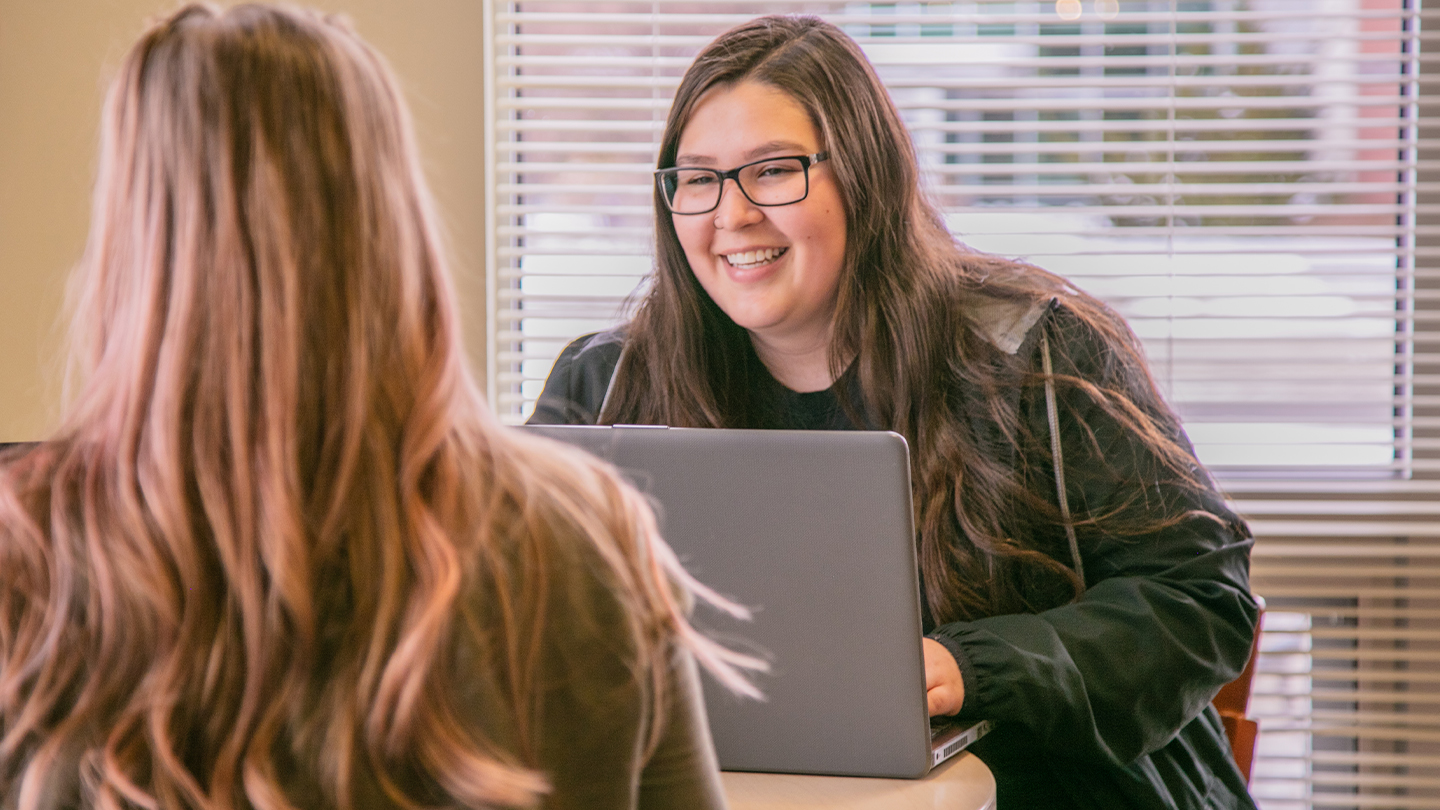 Student at laptop talking with another student across the way