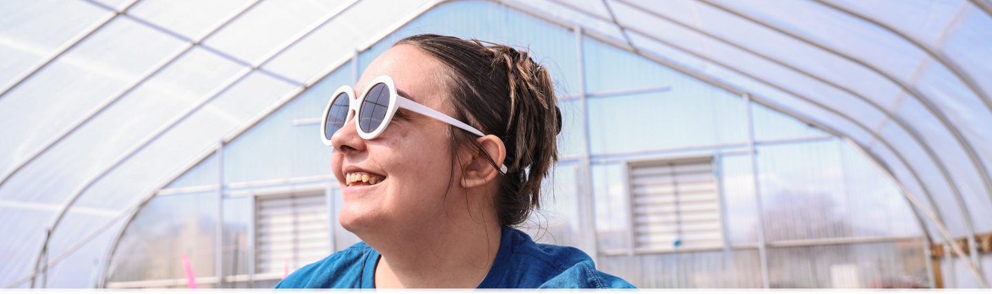 Student smiling at the camera hanging out in a greenhouse on campus!