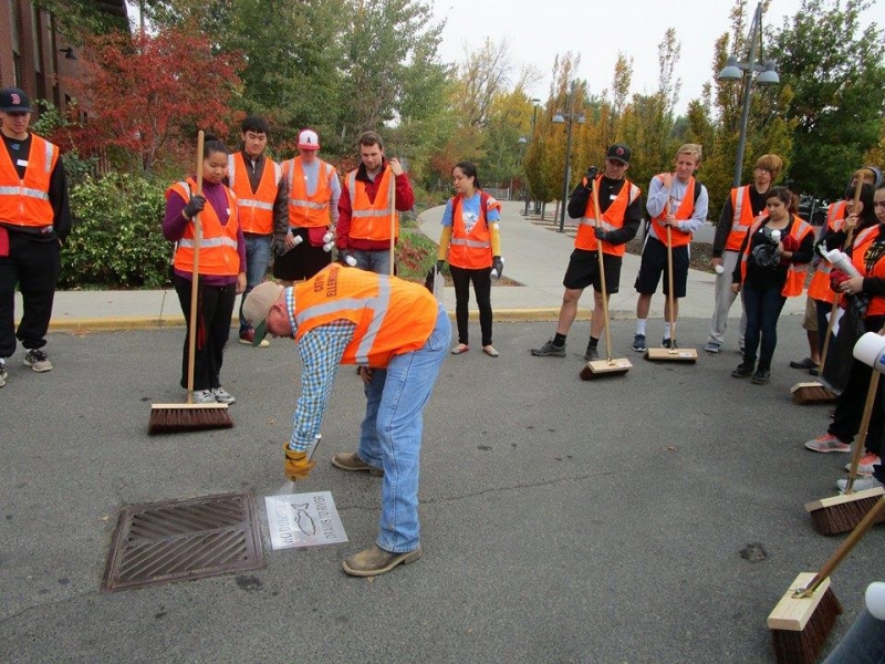 Students standing around a storm drain in oranges vests.