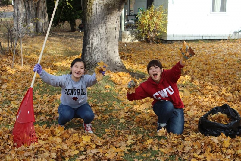 2 students surrounded by leaves with rakes in hand