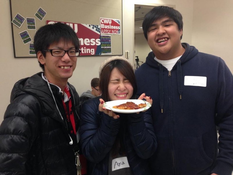 3 students smiling at the camera, one is holding food.