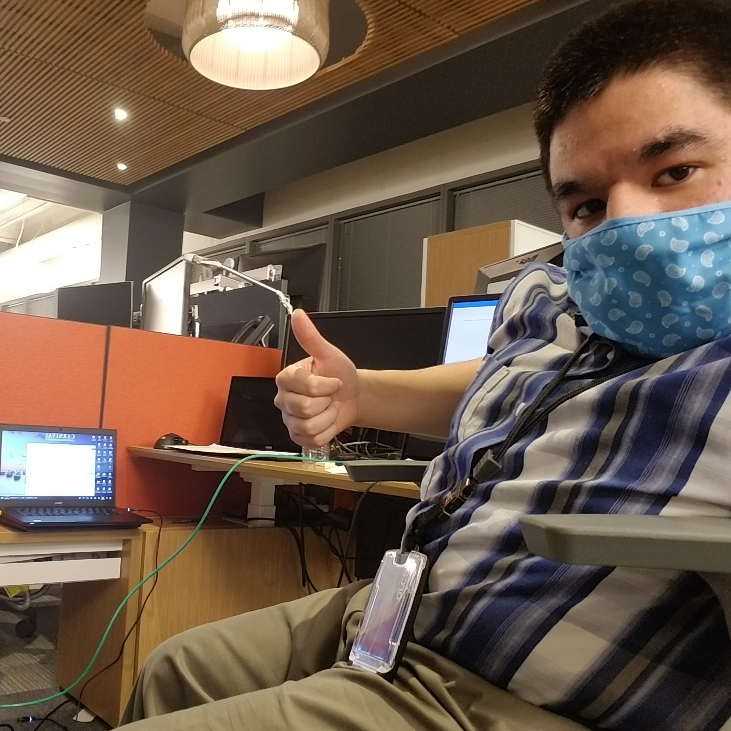 Joseph sitting at a desk holding a thumbs up. There is a computer on the desk