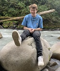 Alex Dupuis sitting on a rock. He is wearing a blue t-shirt