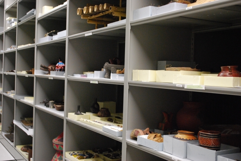 Grey museum storage shelves with blue and tan boxes containing pottery, masks, and other museum objects. 