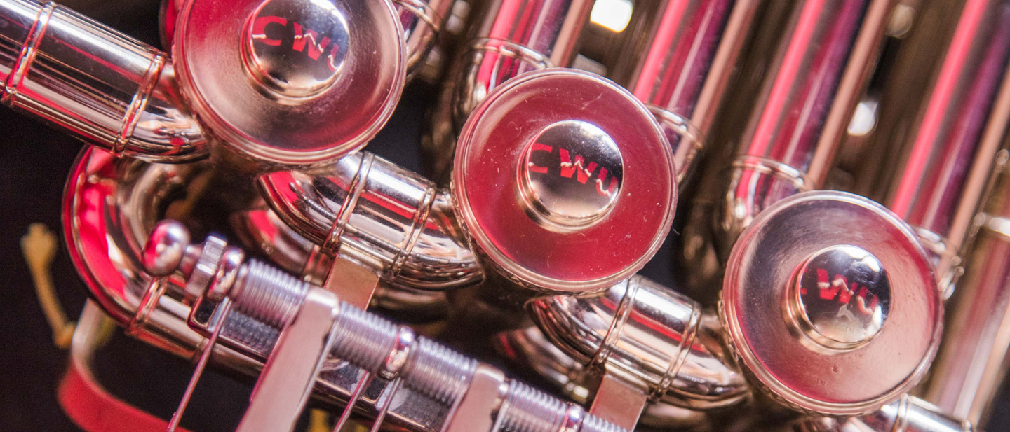 Close up image of French horn valve reflecting the CWU logo in a crimson hue.