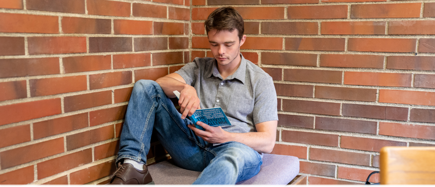 Student sitting in a corner, reading a book.