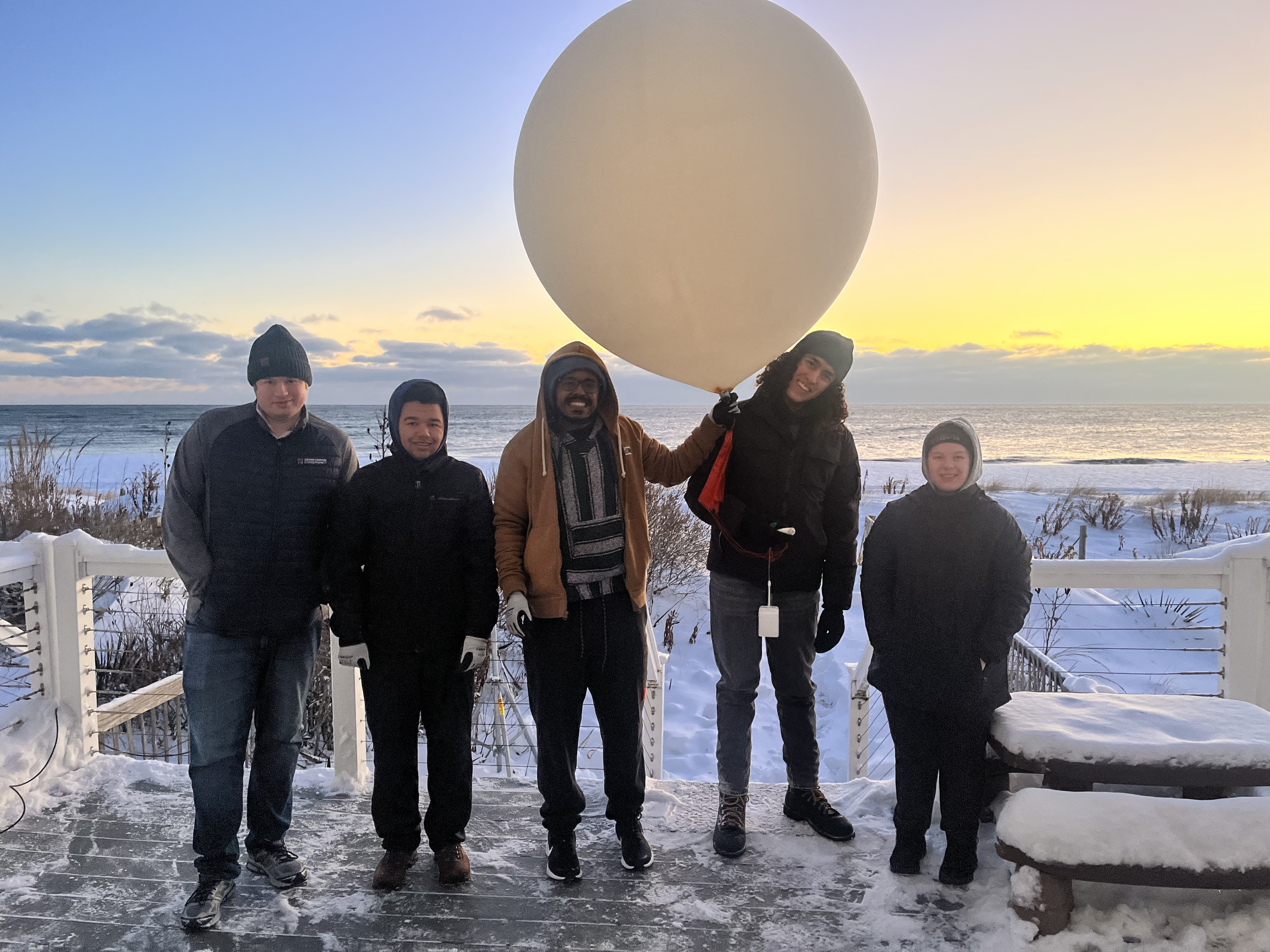 Smiling students with a large balloon in the center.