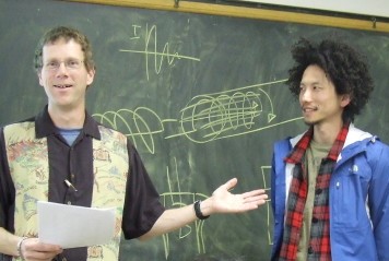 Dr. Palmquist and guest in front of a chalkboard with helical drawings on it.