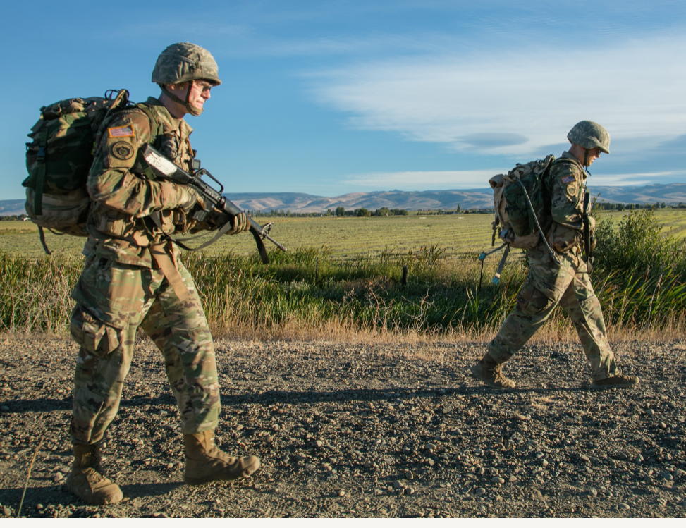 ROTC students walking with guns on a gravel road