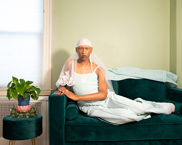 Artist Golden posed in white and lace attire across a loveseat.