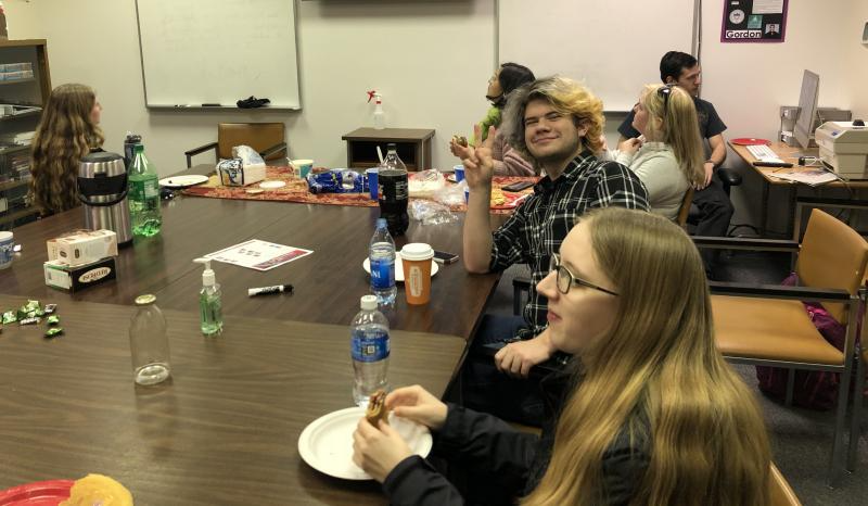 A picture of a Russian Club Meeting. Two people are eating at a large table and one of them is holding up a peace sign.