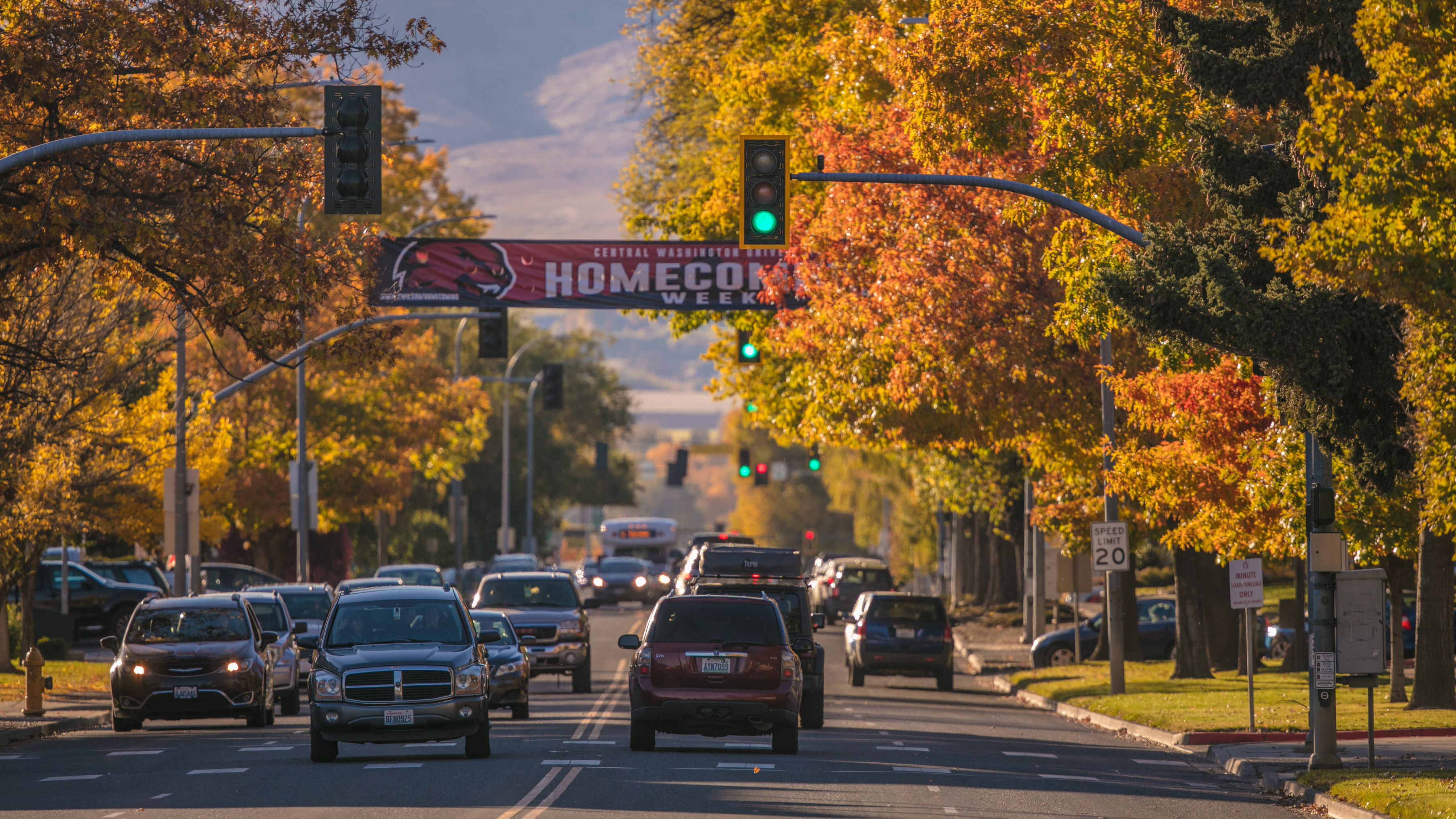 An image of a street in Ellensburg. There is a banner over traffic that says "Central Washington University Homecoming Weekend" and the trees around the road are fall colors, orange and green.
