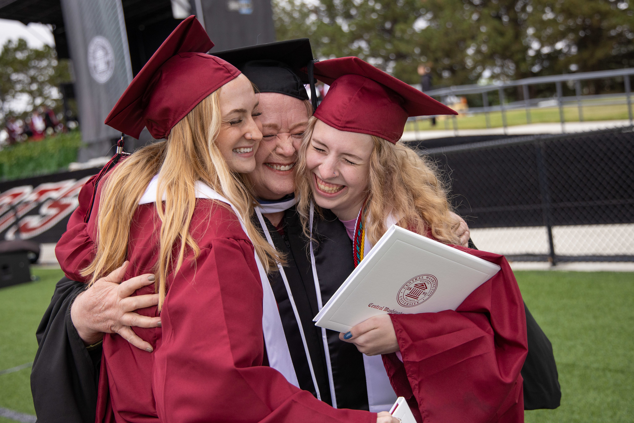 Retired professor Terri Reddout hugs two students at the 2023 commencement ceremony
