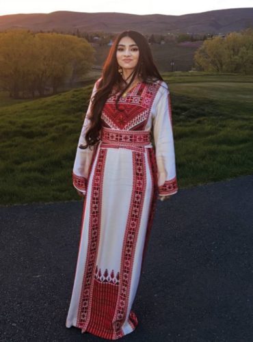 Fatima Taha posing in front of a field, wearing a white and red outfit with traditional patterns.