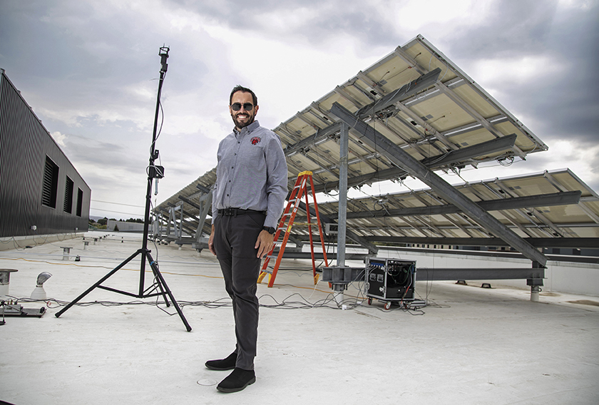 Greg Lyman standing next to solar panels on a windy day on the Hogue Hall roof.