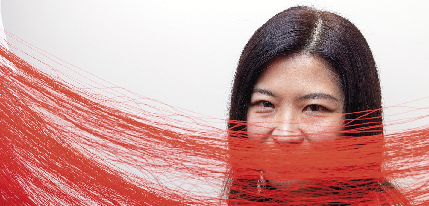 Art Professor Kate Im stands behind a red thread sculpture