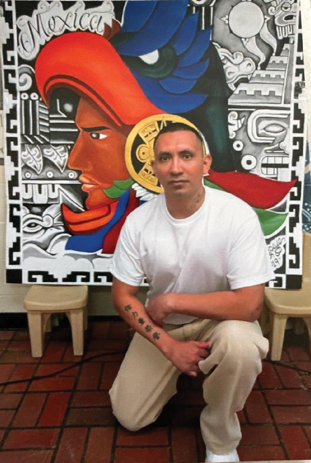 Luis Moreno kneeling in front of artwork in prison