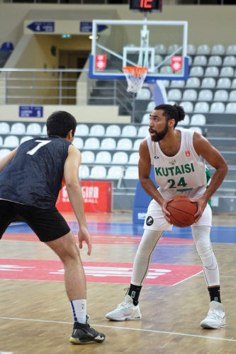 Marqus Gilson with basketball in hand while the other team's player trying to block him.