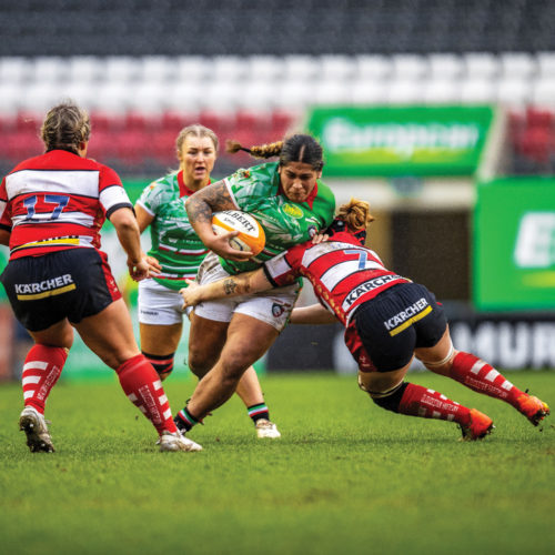 One rugby player tries to tackle another one, while two others watch from a short distance.