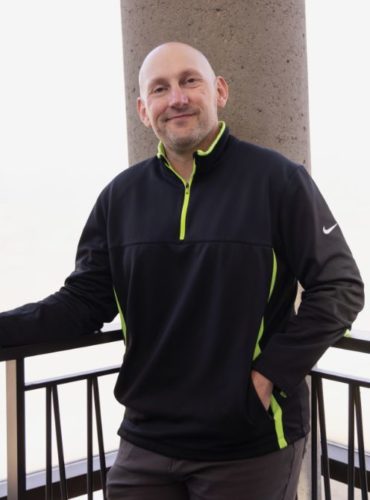 Tim Booth posing in front of a concrete column and metal railing.
