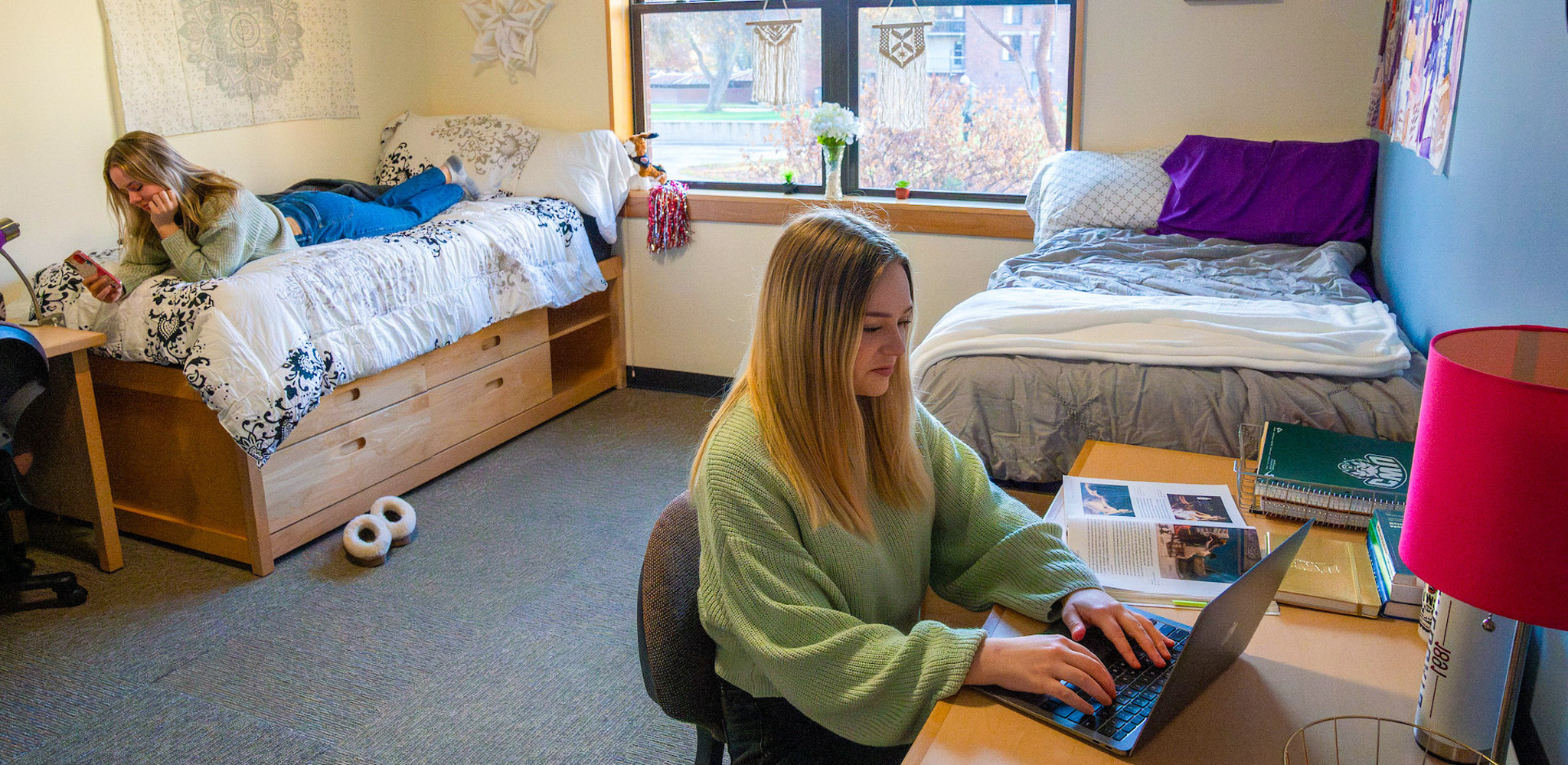 Two students in their room studying and sitting on the bed