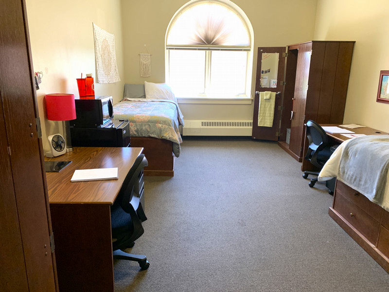 A room with a window in the middle and a bed, desk, and closet on each side