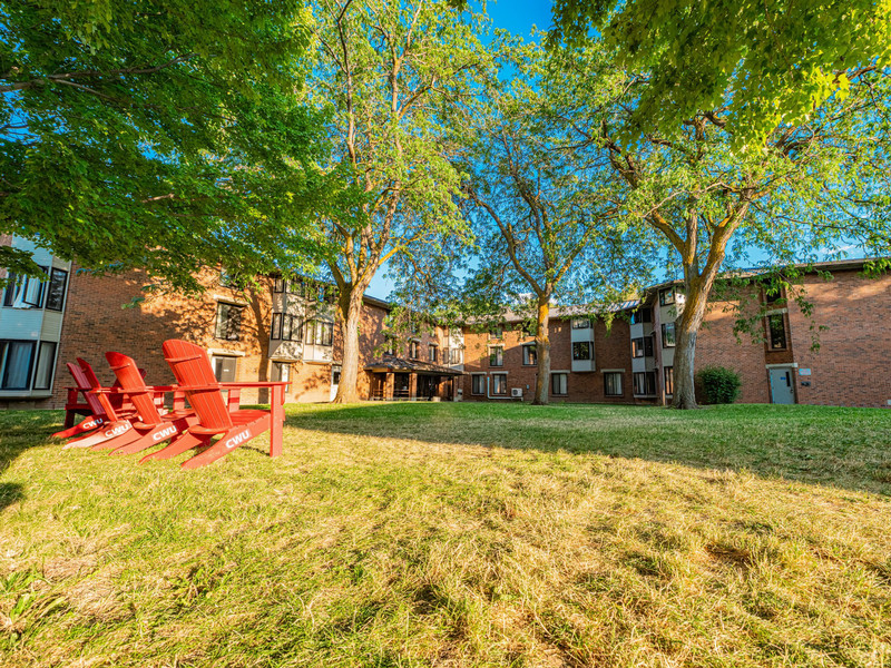 Brick three-story residence hall in the summer time with red lawn chairs in front