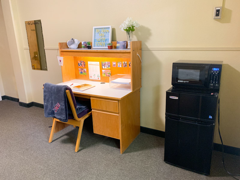 Desk and desk chair next to microwave and fridge unit